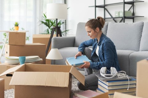 Donna che organizza libri e oggetti personali in salotto con scatole