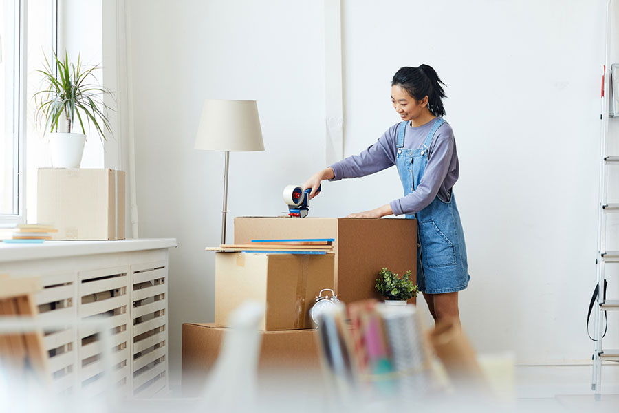 Young woman sealing a cardboard box with packing tape in a bright room