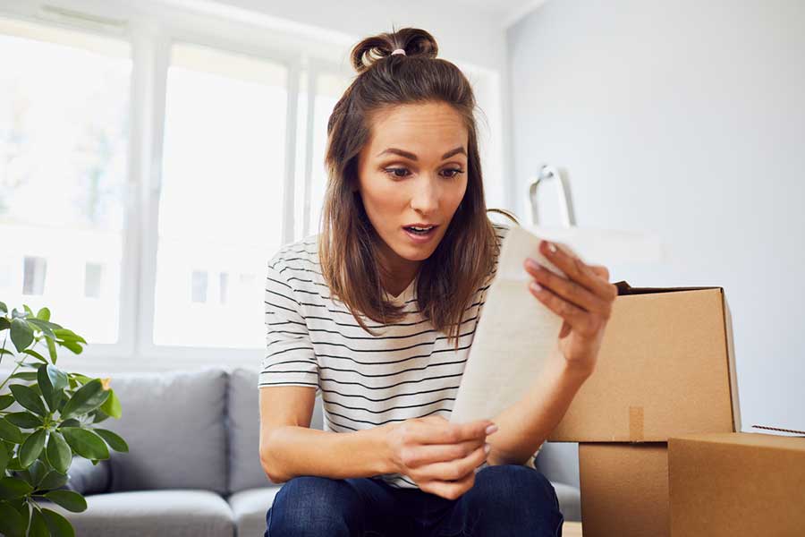 Donna con scatole da trasloco sullo sfondo mentre controlla i costi del trasferimento.