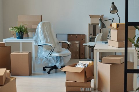 Office space filled with cardboard boxes and wrapped furniture during a relocation.
