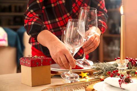 Persona che apparecchia la tavola con bicchieri e decorazioni natalizie