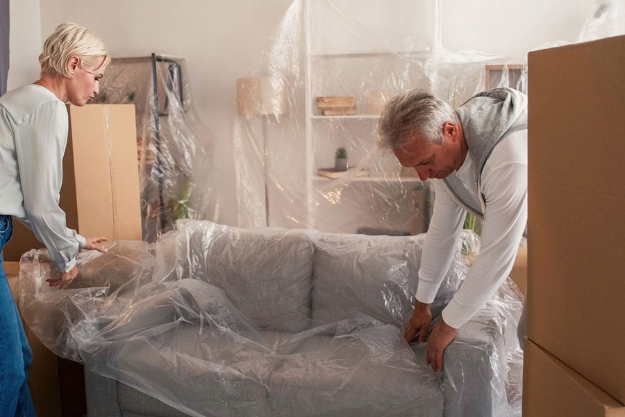 Couple covering furniture with protective plastic sheeting in preparation for moving
