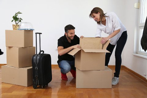 Smiling couple packing belongings into cardboard boxes in an empty room