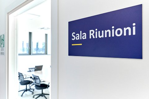 Modern office meeting room with open door and a sign reading 'Sala Riunioni'.