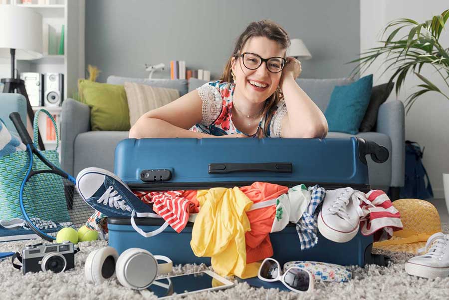 Donna sorridente accanto a una valigia strapiena pronta per le vacanze